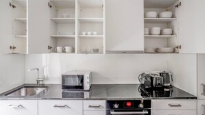 A modern kitchen with white cabinets, a black countertop, a Bosch microwave, a coffee machine, and an oven. - Superb St. Johann 1BR w/ Storage Room, close to Station, by Blueground (Basel)