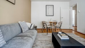 A modern living room with a grey sofa, a coffee table, and a dining area with chairs and a table. - Superb St. Johann 1BR w/ Storage Room, close to Station, by Blueground (Basel)
