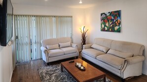 A living room with two striped sofas, a coffee table with candles, a painting on the wall, and a TV mounted on the wall.