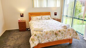 A bedroom with a wooden bed, a nightstand, a bedside lamp, and a window with blinds.