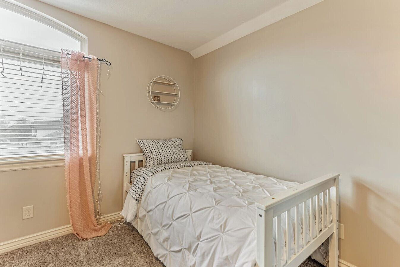 A bedroom with a single bed, a round wall shelf, and a window with blinds.