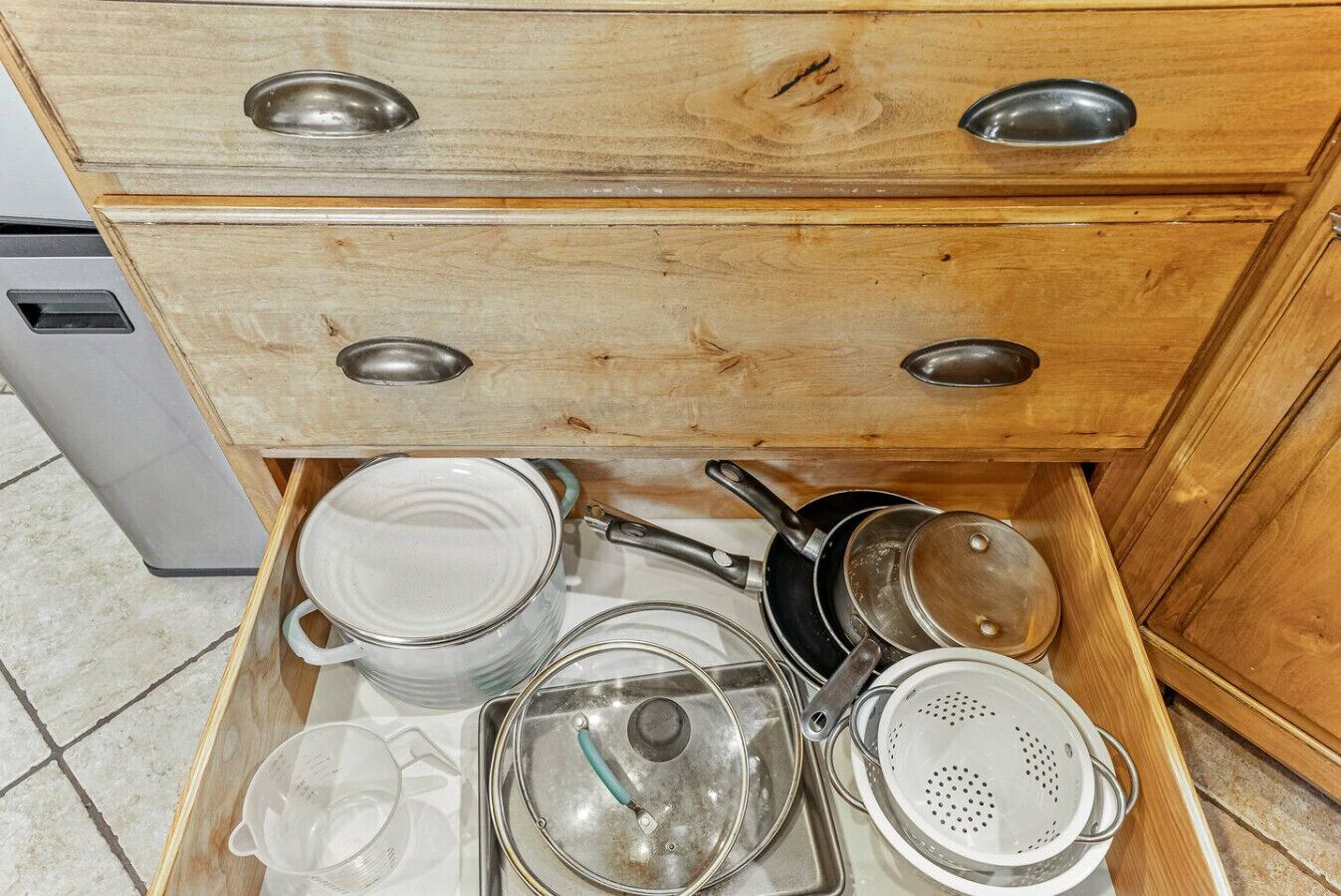 Un cajón de madera con pomos metálicos, que contiene diversos utensilios y utensilios de cocina.