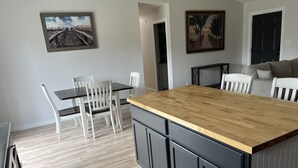 Une cuisine moderne avec un îlot central en bois, des chaises blanches et deux tableaux encadrés accrochés au mur.