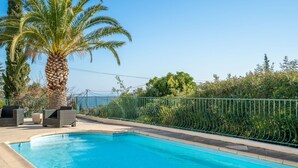 A swimming pool with a curved green metal fence, lounge chairs, and a palm tree. - Les Chèvrefeuilles by Interhome (Saint Aygulf)