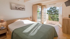 A bedroom with a bed, a nightstand, a lamp, a painting, and a balcony with a view of trees. - Les Chèvrefeuilles by Interhome (Saint Aygulf)