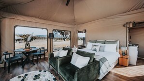 Une pièce aménagée sous une tente, avec un lit, un canapé, une table et une vue sur le paysage désertique.