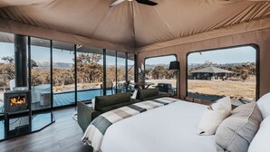 Une vaste pièce aménagée sous une tente, avec un lit, une cheminée et une vue sur le paysage.