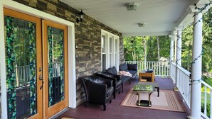 A covered porch with a stone wall, black leather furniture, and a view of a wooded area.