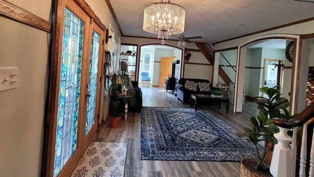 A spacious hallway with a chandelier, wooden floors, and a patterned rug.