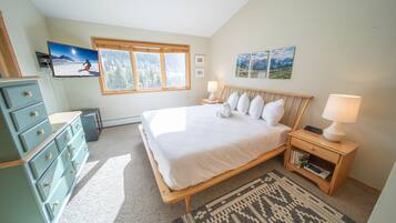 Un dormitorio con cama, mesitas de noche, cómoda, televisor y ventana con vista a las montañas.