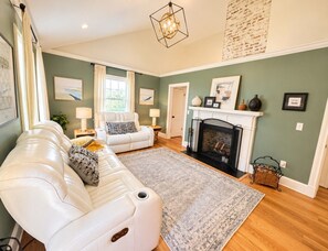 A living room with a fireplace, a white sofa, a patterned rug, and artwork on the walls. - Downtown Sptg Historic Pet Friendly Home Sleeps 4 (Spartanburg)