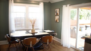 Un coin repas avec une table et des chaises, un vase décoré de branches et une vue sur un balcon agrémenté d’un canapé.