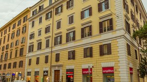 A multi-story yellow building with a corner entrance, storefronts on the ground floor, and a visible sign for 'amplifon'.