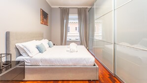 A modern bedroom with a large bed, a bedside table, a window with curtains, and a cityscape view.