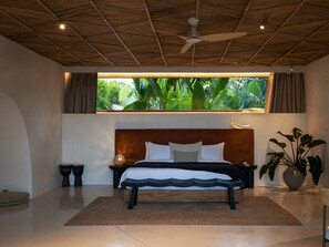 A bedroom with a bed, a ceiling fan, a window with curtains, a nightstand, a lamp, and a potted plant.