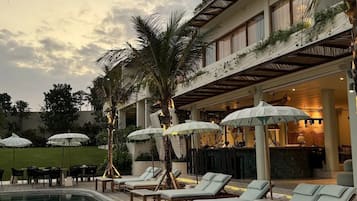 A poolside area with lounge chairs and umbrellas, a pool, and a building with a covered patio.