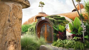 A unique building with a large wooden door, surrounded by lush greenery and a small tree on top. - Oshom Bali at Nuanu Creative City (Tabanan)