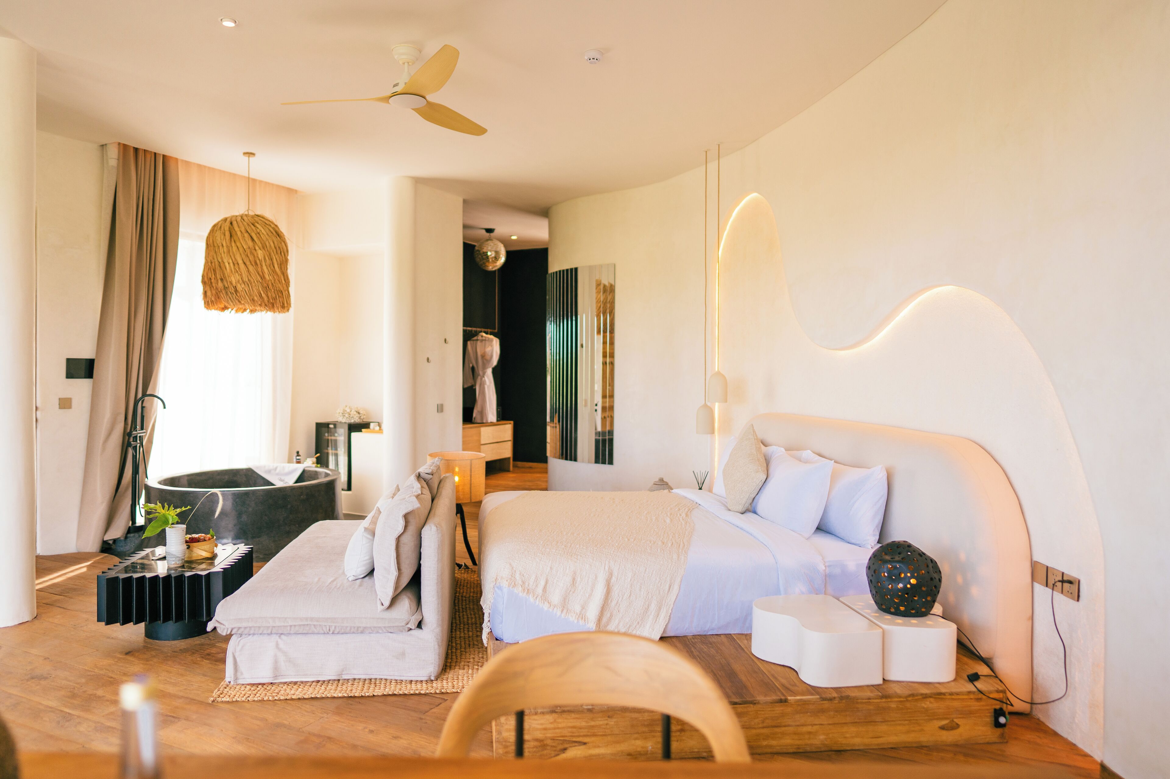 Un dormitorio moderno con una cama grande, un área de descanso con una silla, una mesita y un ventilador de techo.