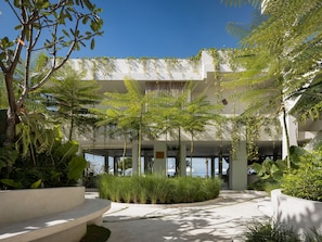 Un edificio moderno con un área exterior cubierta que incluye macetas con diversas plantas y una vista despejada del cielo.