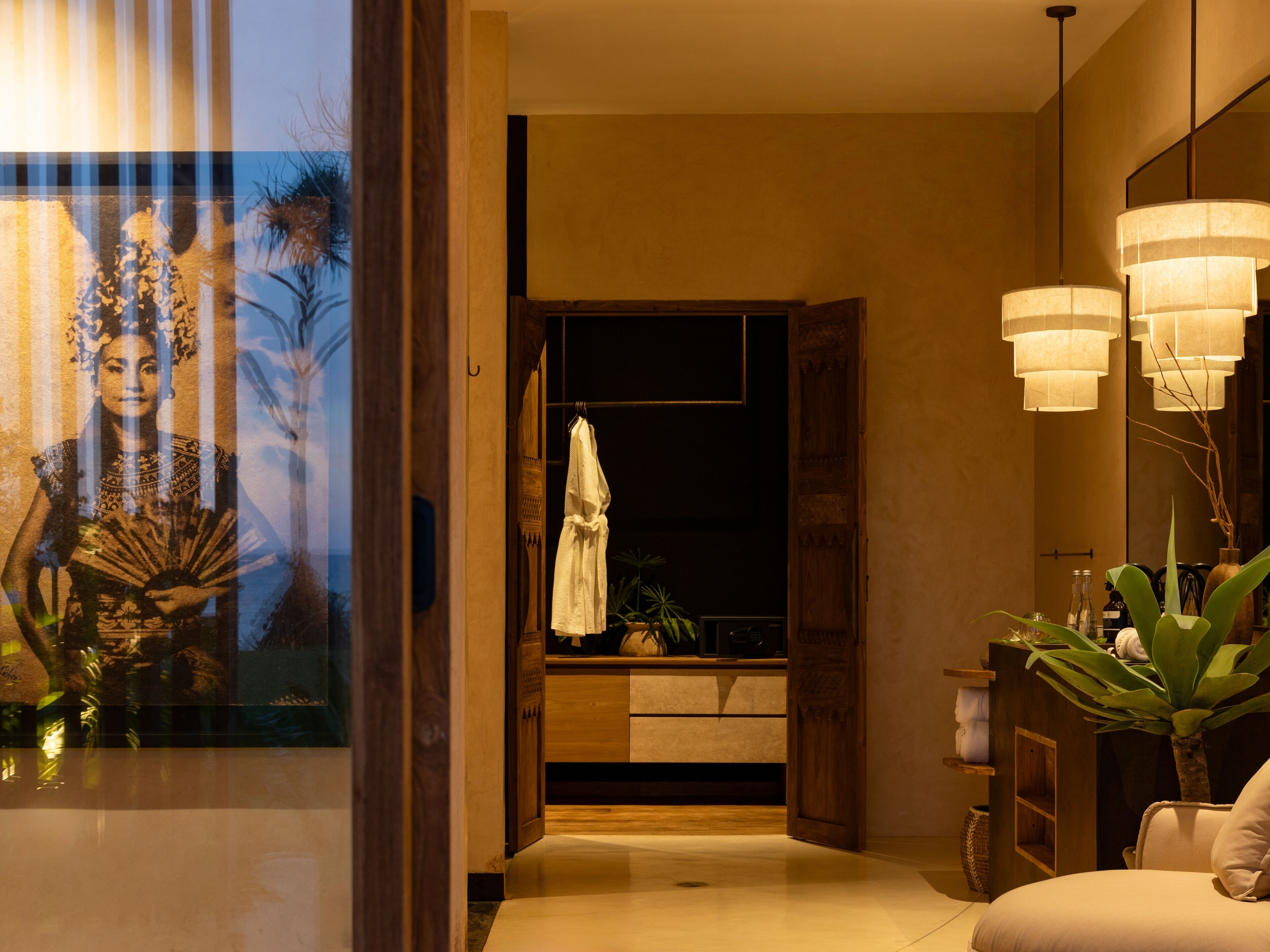 A modern hotel lobby with a wooden reception desk, a large mirror, and a seating area with a sofa and plants.