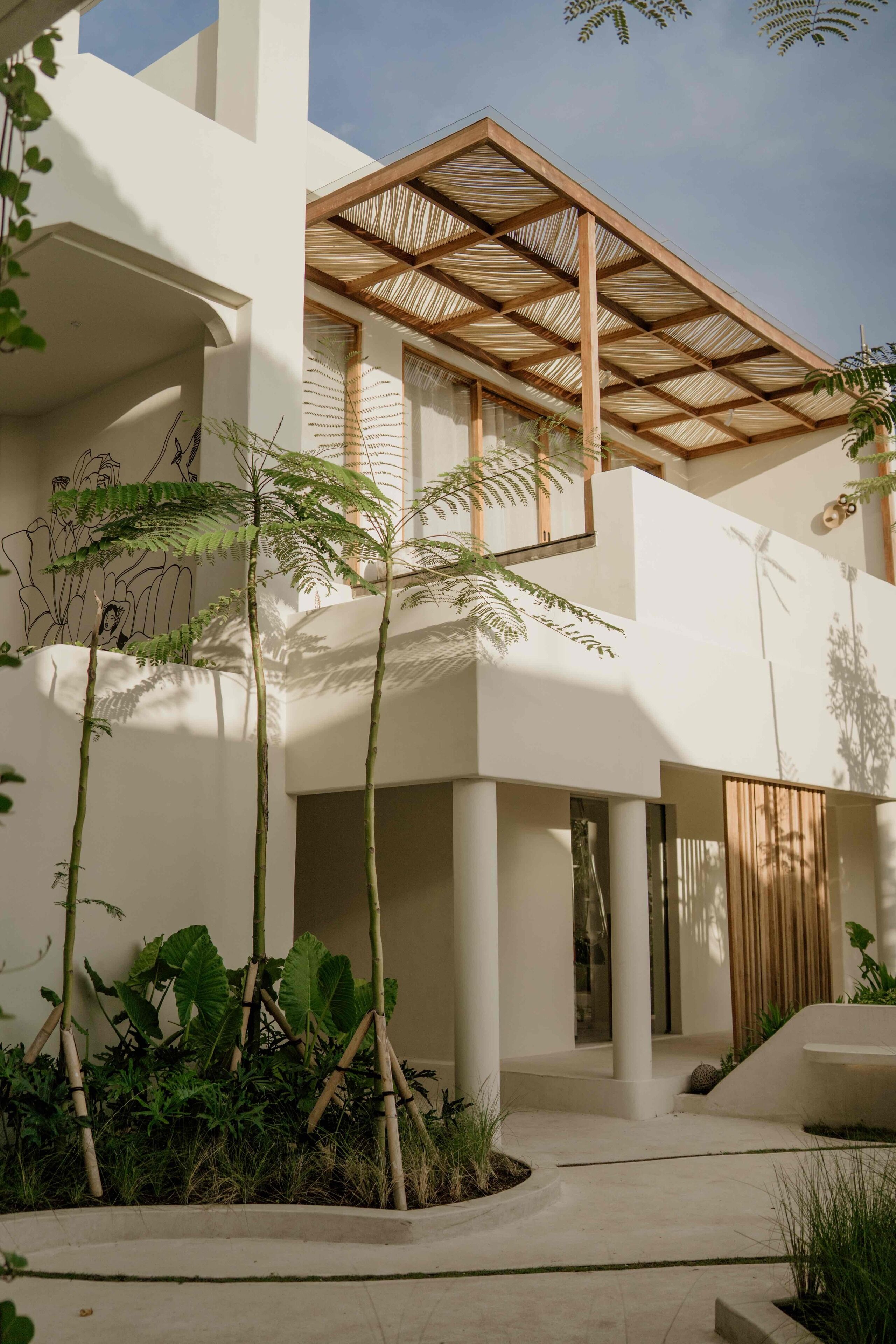 A modern building with a covered outdoor area, columns, and greenery.