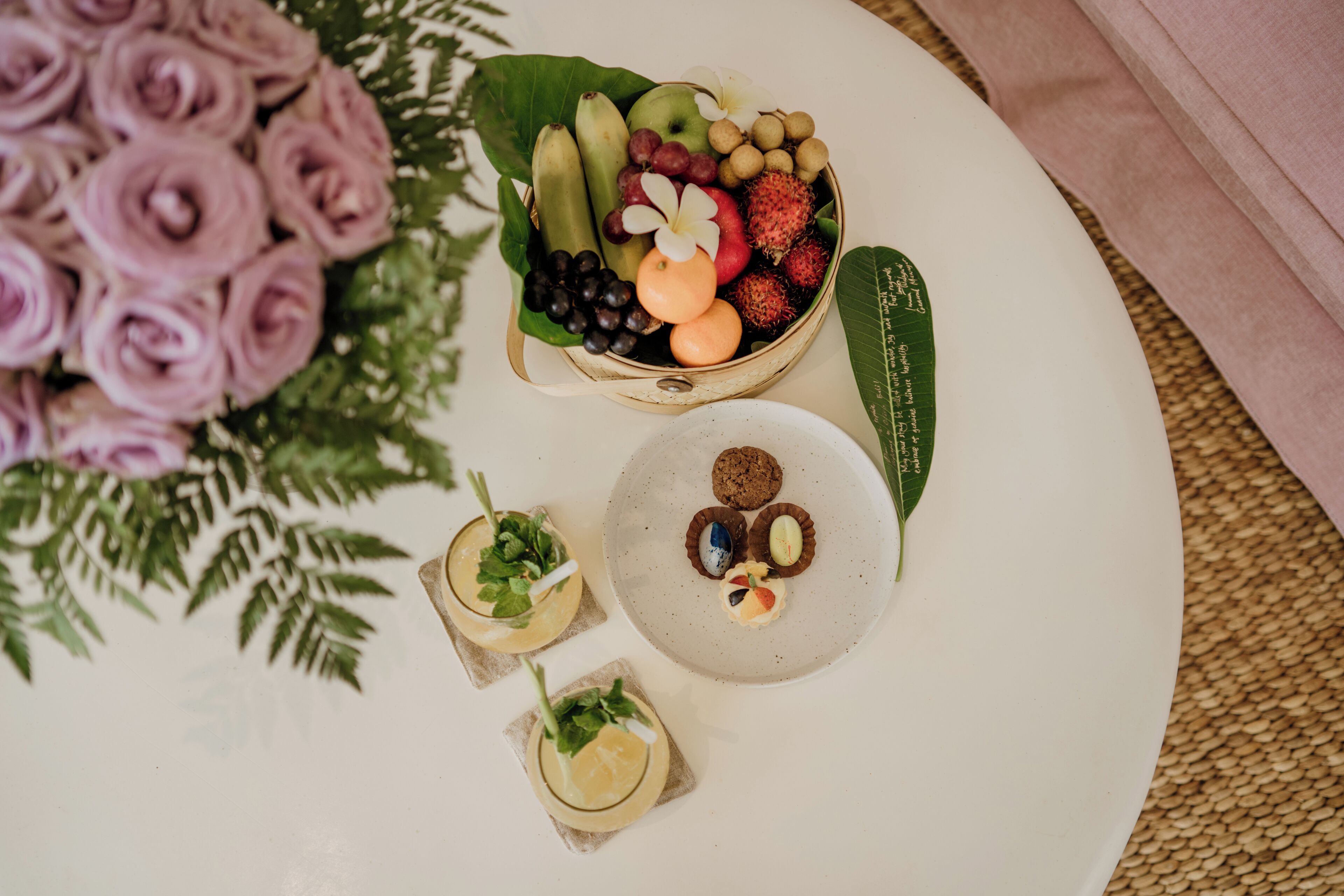 A table with a fruit and dessert arrangement, a plate with cookies, and a floral arrangement.
