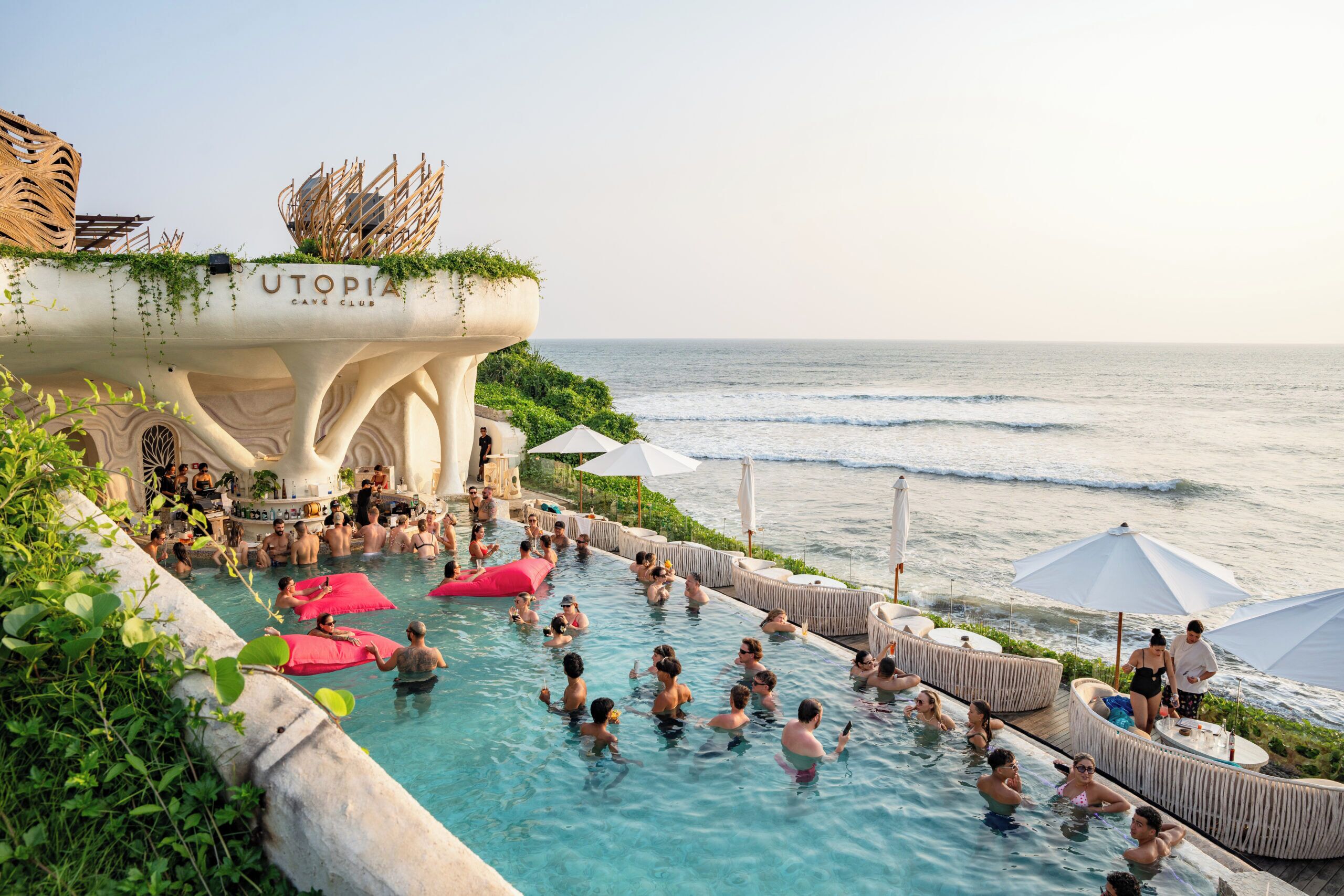 A pool area with people swimming, a bar, and a view of the ocean.