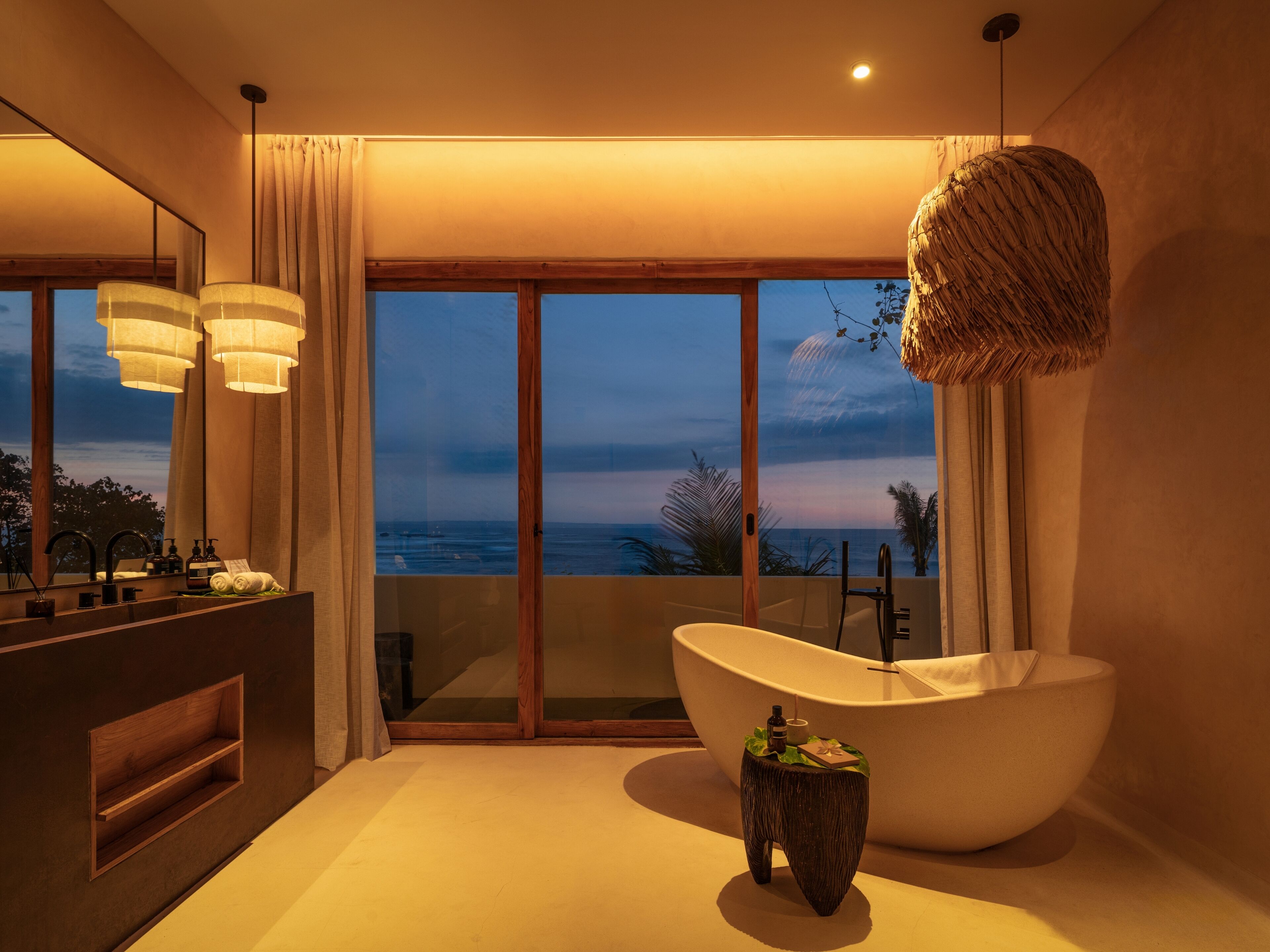 A modern bathroom with a freestanding bathtub, a vanity with a mirror, and a view of the ocean.