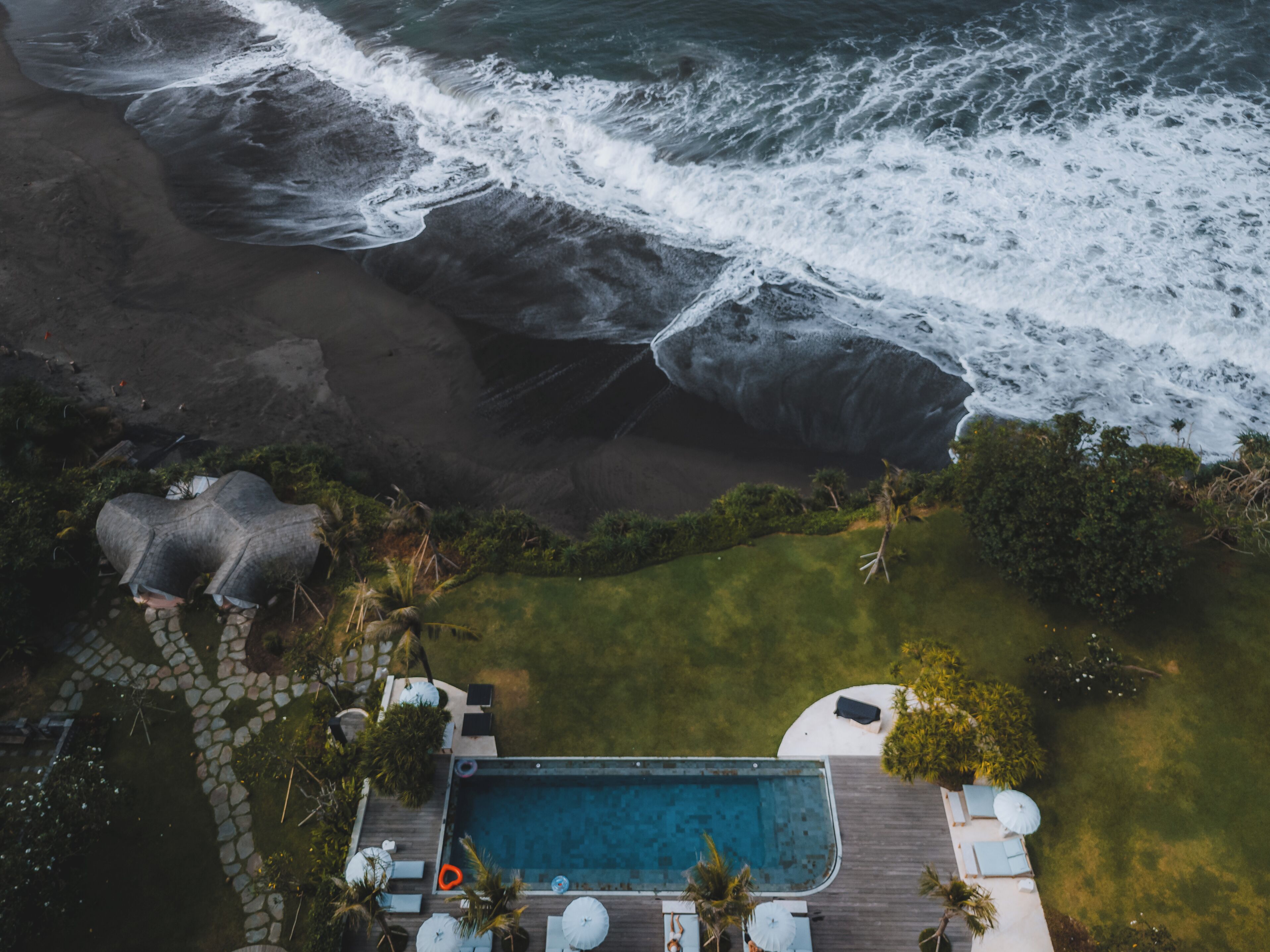 An aerial view of a beachfront property with a swimming pool, lounge chairs, and a garden area.