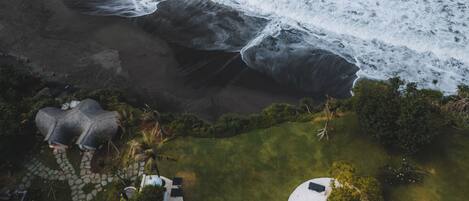 An aerial view of a beachfront property with a swimming pool, lounge chairs, and a garden area.