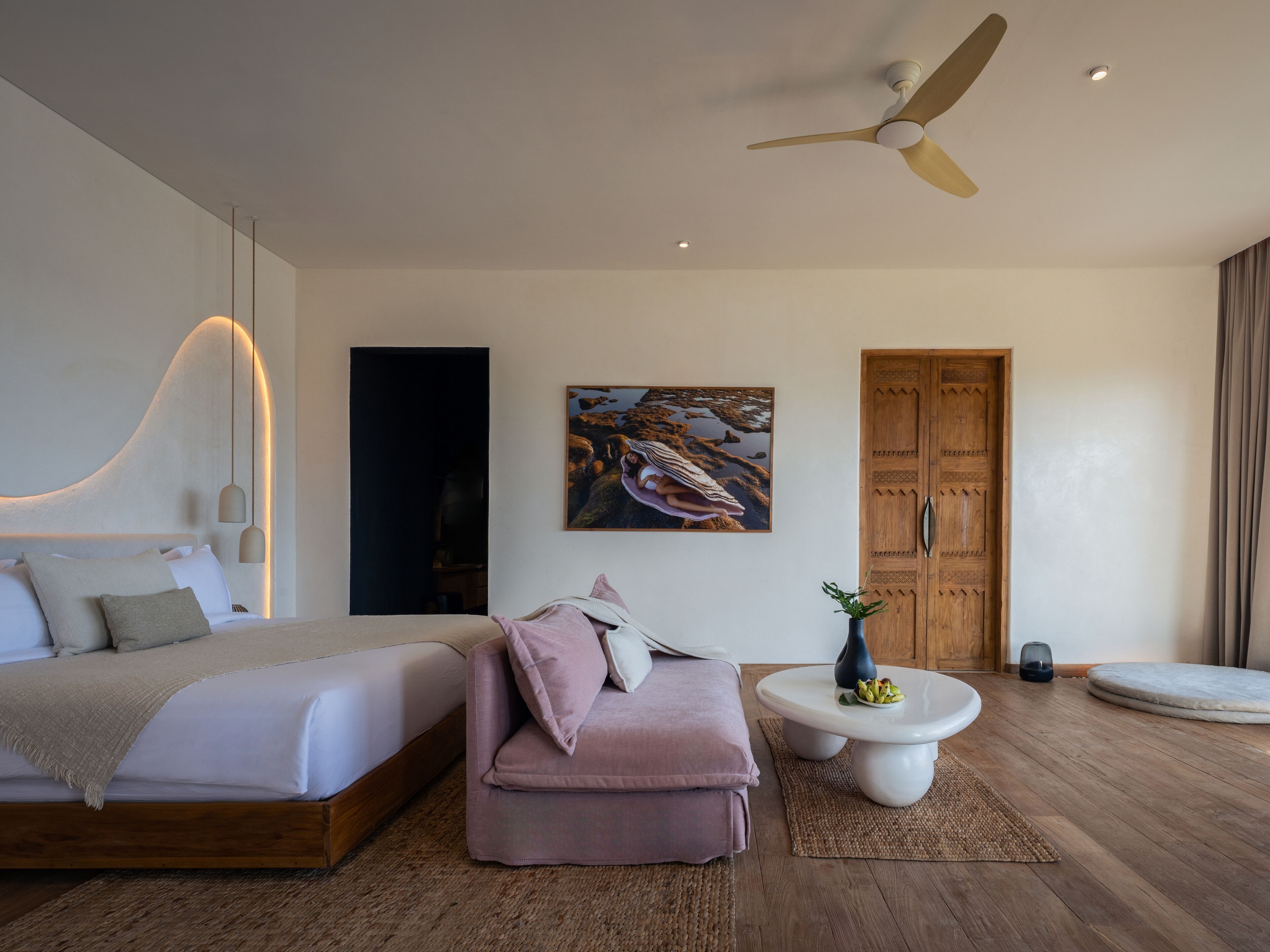A modern bedroom with a bed, a sofa, a coffee table, and a ceiling fan.