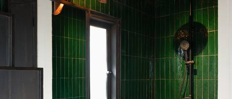 Un bagno con parete rivestita in piastrelle verdi, una panca in legno, un lavabo spazioso con una bacinella intrecciata e una doccia con soffione a mano.