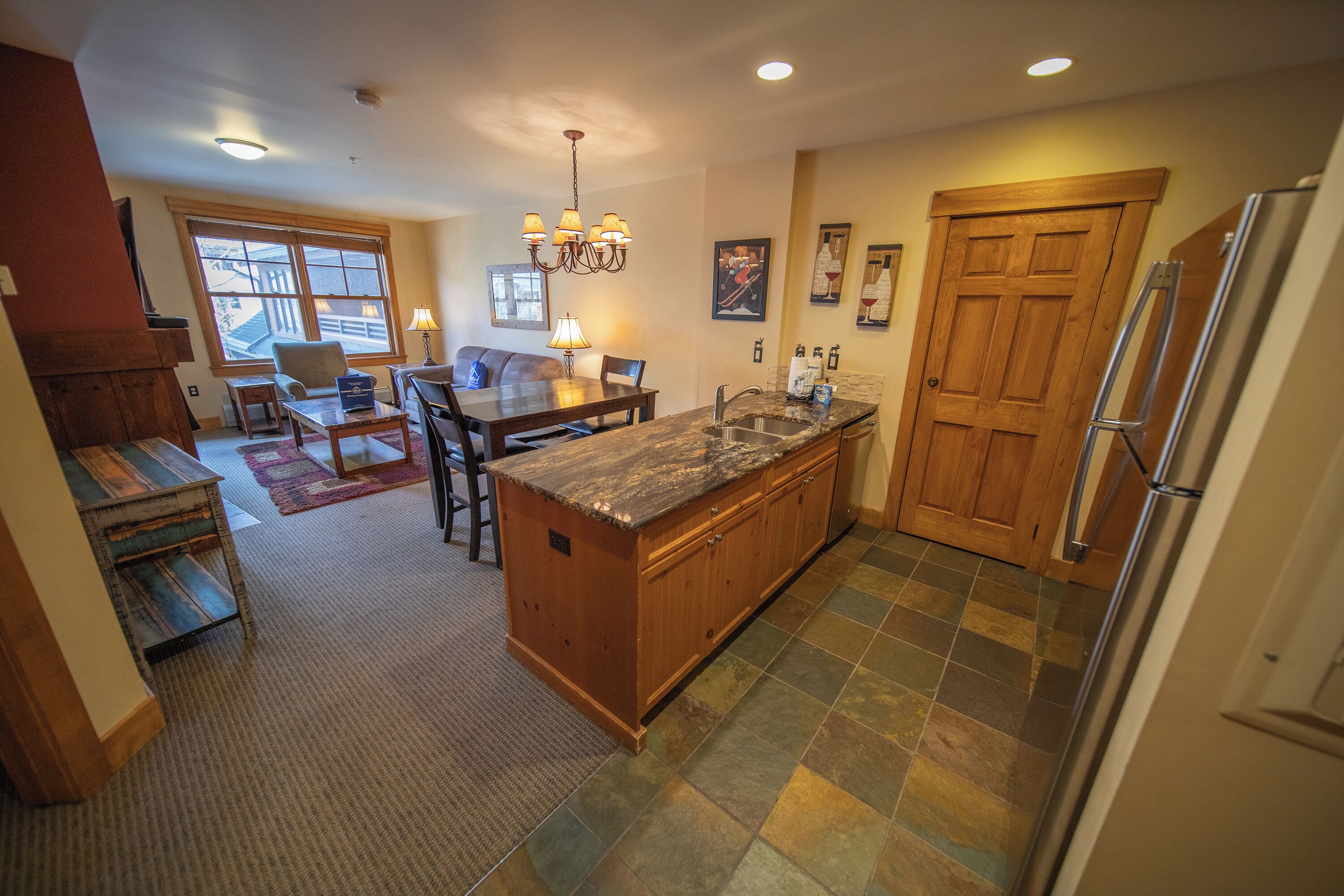 A kitchen with a large island, wooden cabinets, a chandelier, and a refrigerator.