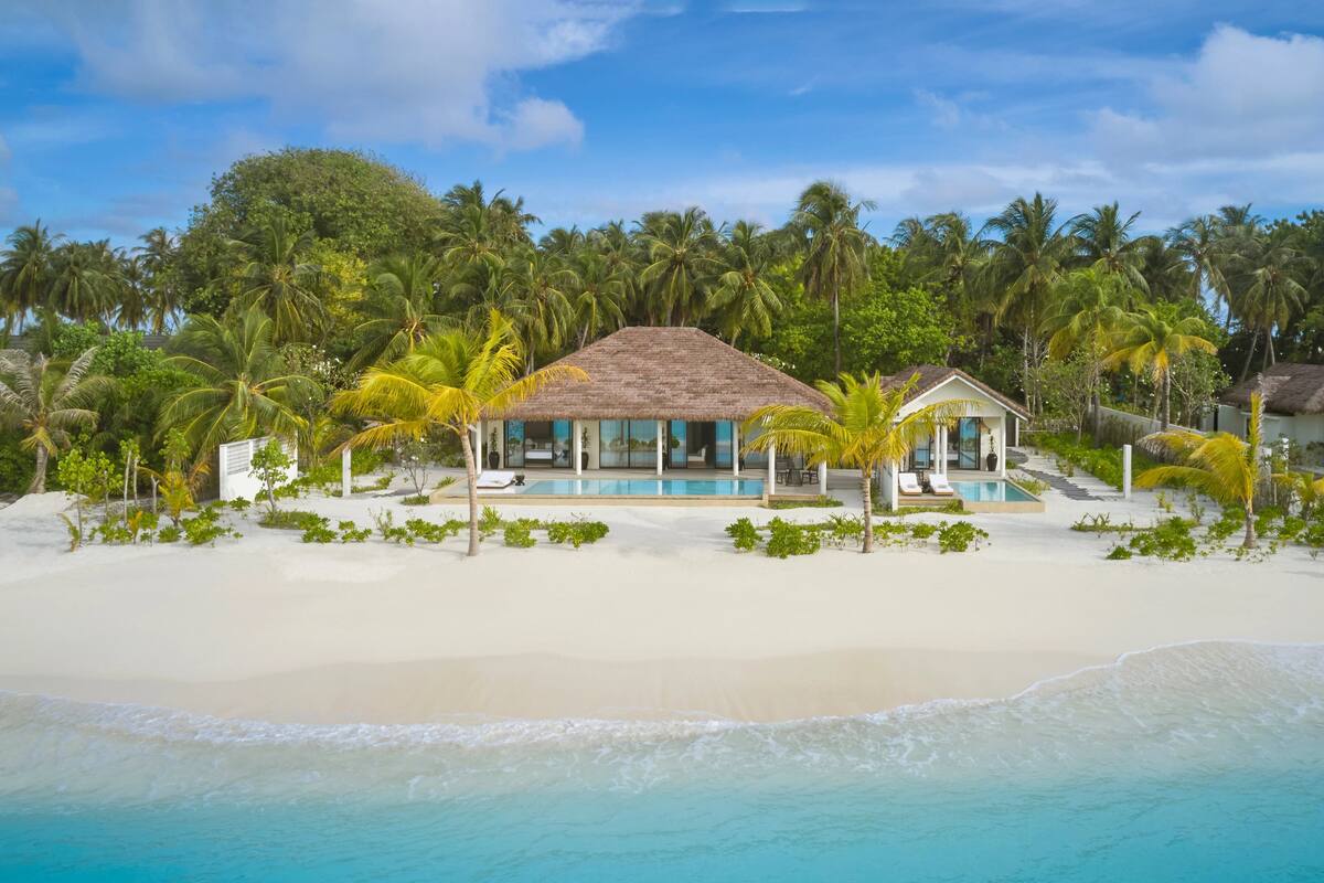 A beachfront property with a pool, palm trees, and a thatched-roof building.
