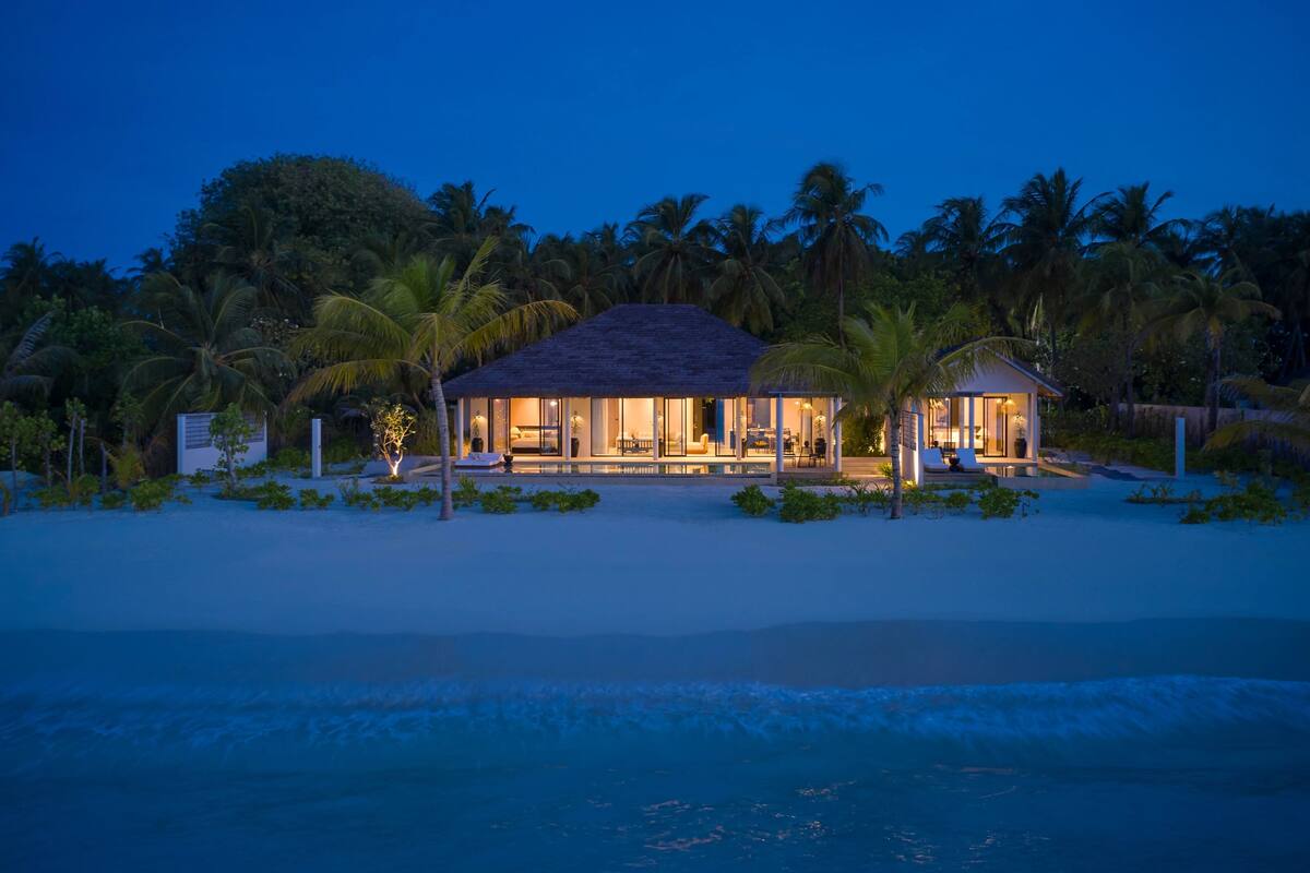 A beachfront resort with a large open patio, palm trees, and a pool.