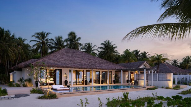 Un resort con piscina, edifici a tetto di paglia e palme.