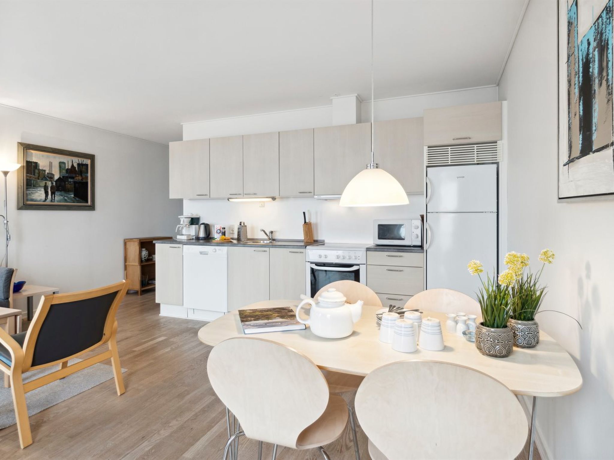 Une cuisine moderne avec des meubles blancs, un coin repas comprenant une table et des chaises, et un luminaire suspendu.