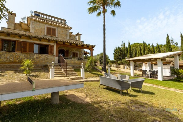 Eine Steinvilla mit überdachter Terrasse, Sitzgelegenheiten im Freien und einer Treppe zum Eingang.