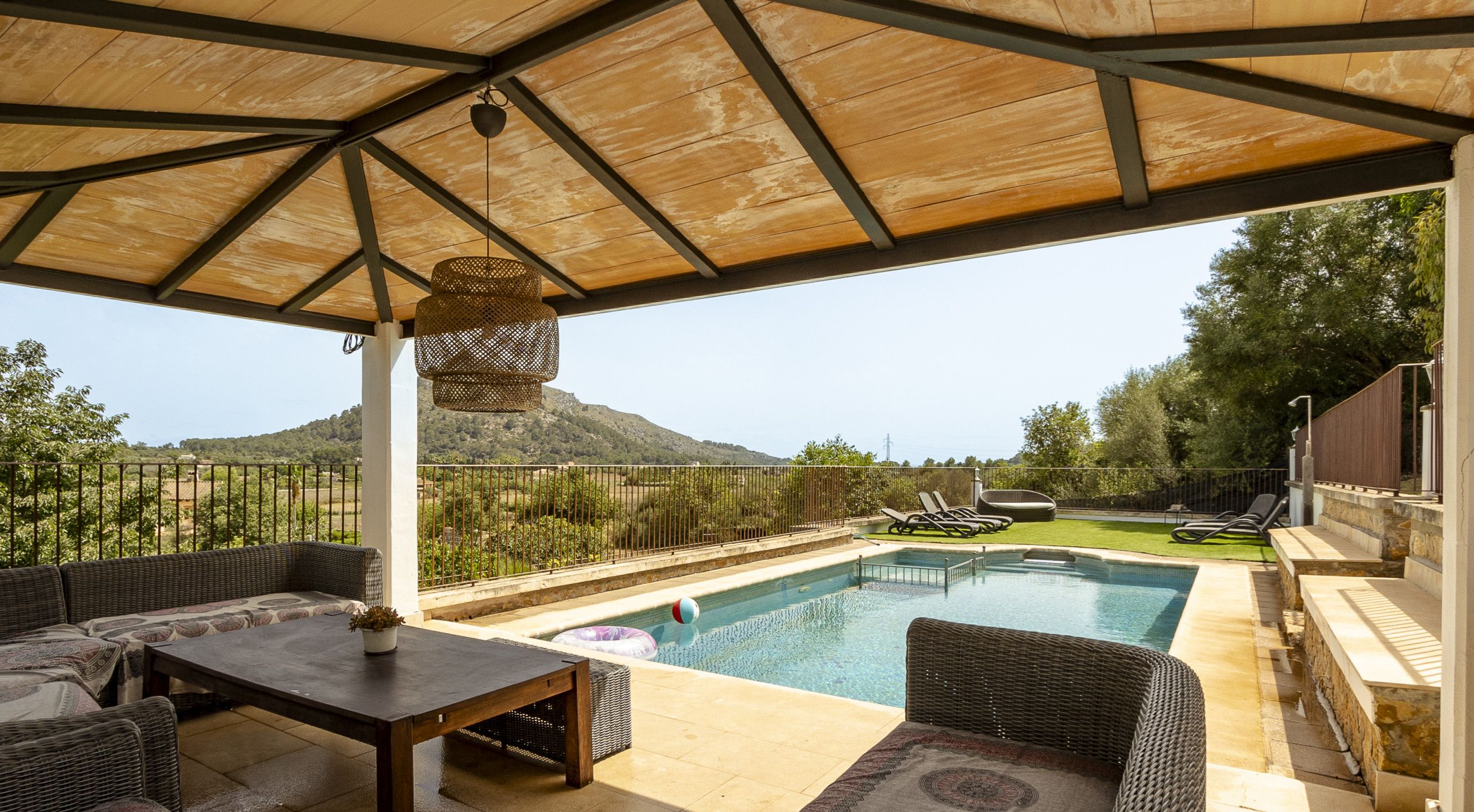 Un espacio al aire libre techado con piscina, mobiliario de mimbre y vistas a la montaña.