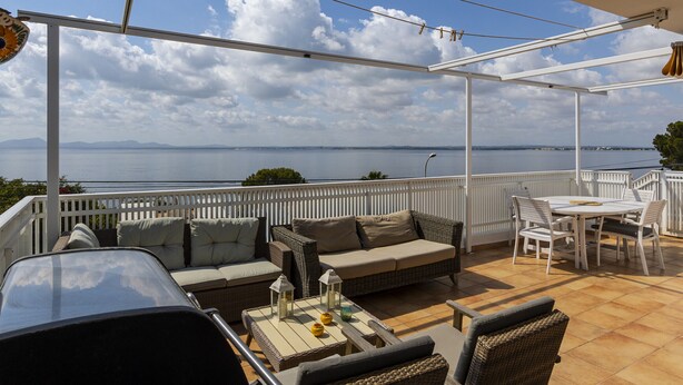 A covered outdoor seating area with a view of the sea, a white fence, and a table with chairs. - Villa Maria by Mallorca North Villas (Alcudia)