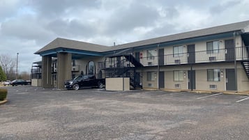 Een motel met twee verdiepingen, een overdekte parkeerplaats en een trap naar de bovenverdieping.