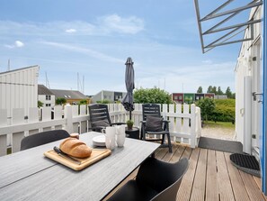 Une terrasse avec une table dressée pour les repas, des chaises d’extérieur et un grand parasol.