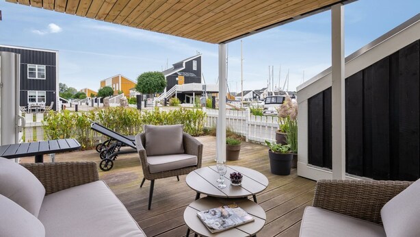 A covered outdoor seating area with wicker furniture, a table with a magazine, and a view of a marina with boats.