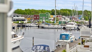 A marina with various boats docked, surrounded by colorful buildings and a forested background.