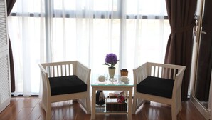 Une pièce avec deux chaises blanches dotées de coussins noirs, une petite table en verre ornée d’un vase de fleurs violettes, et une vue à travers des rideaux transparents.