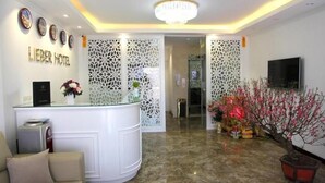 Un hall d’accueil d’hôtel avec un comptoir de réception blanc, un lustre et des panneaux décoratifs.
