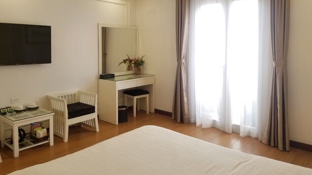 Une chambre d’hôtel avec un grand lit, un bureau avec une chaise, un téléviseur fixé au mur et une fenêtre avec des rideaux.