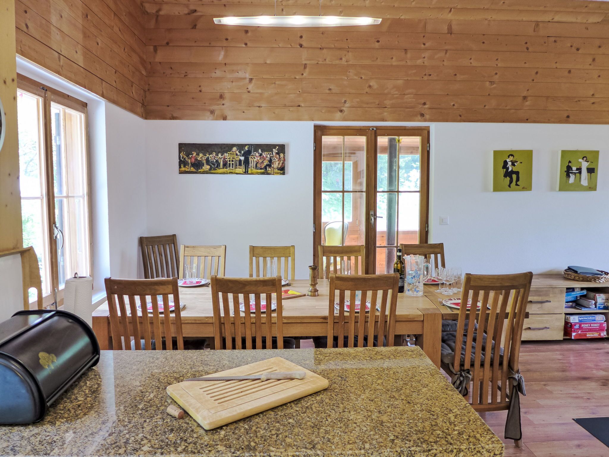 A dining area with wooden chairs and a granite table, featuring a painting and a door leading outside.