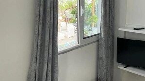 A room with a large window, a flat-screen TV on a white stand, and a white wall. - The perfect one bedroom apartment (Sarande)