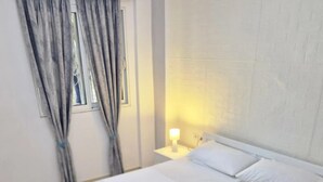 A neatly made bed with white linens, a bedside lamp, and a window with curtains. - The perfect one bedroom apartment (Sarande)